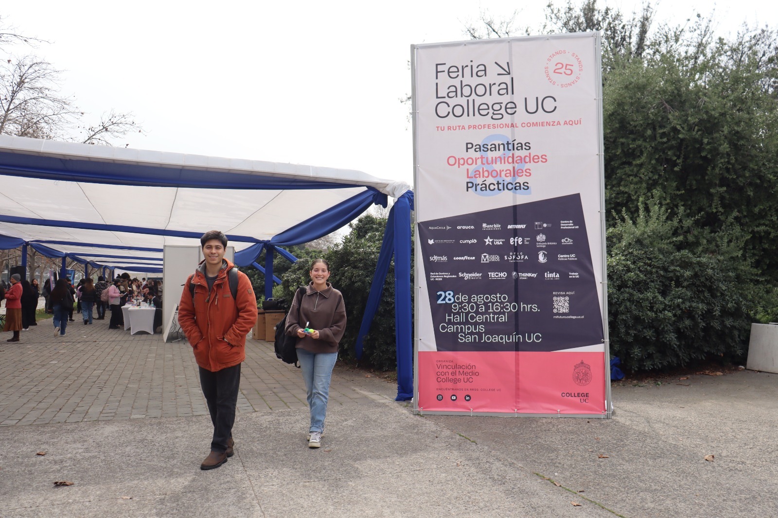Estudiantes ingresan a la Feria Laboral College UC 2025 en el Campus San Joaquín, junto a un cartel con información sobre pasantías, oportunidades laborales y prácticas.